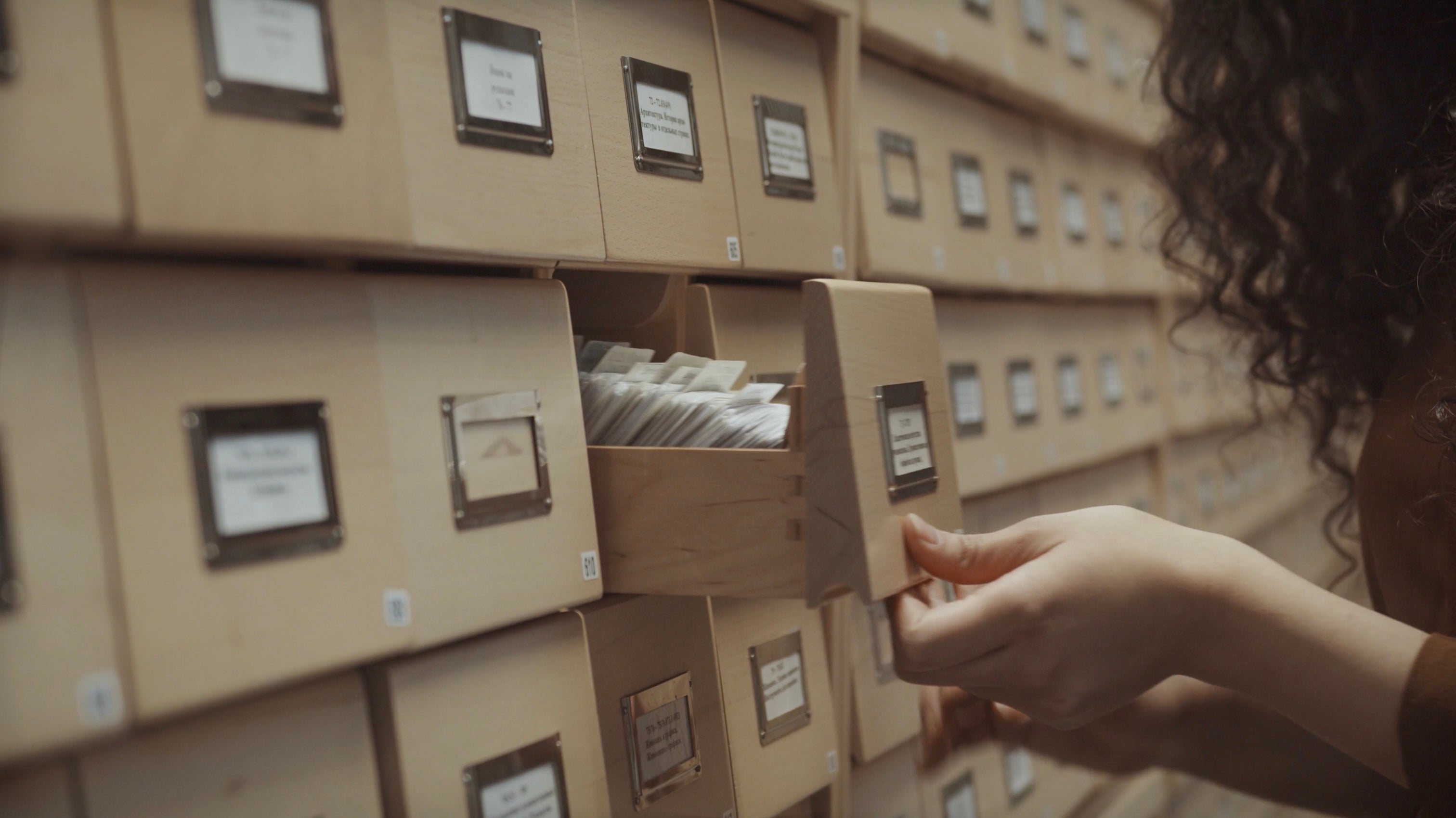 Person selecting a drawer from a shelf of labeled drawers in an archive room.